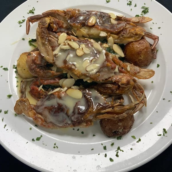 Fried soft-shell crabs topped with sliced almonds and a creamy sauce, served with potatoes and greens.