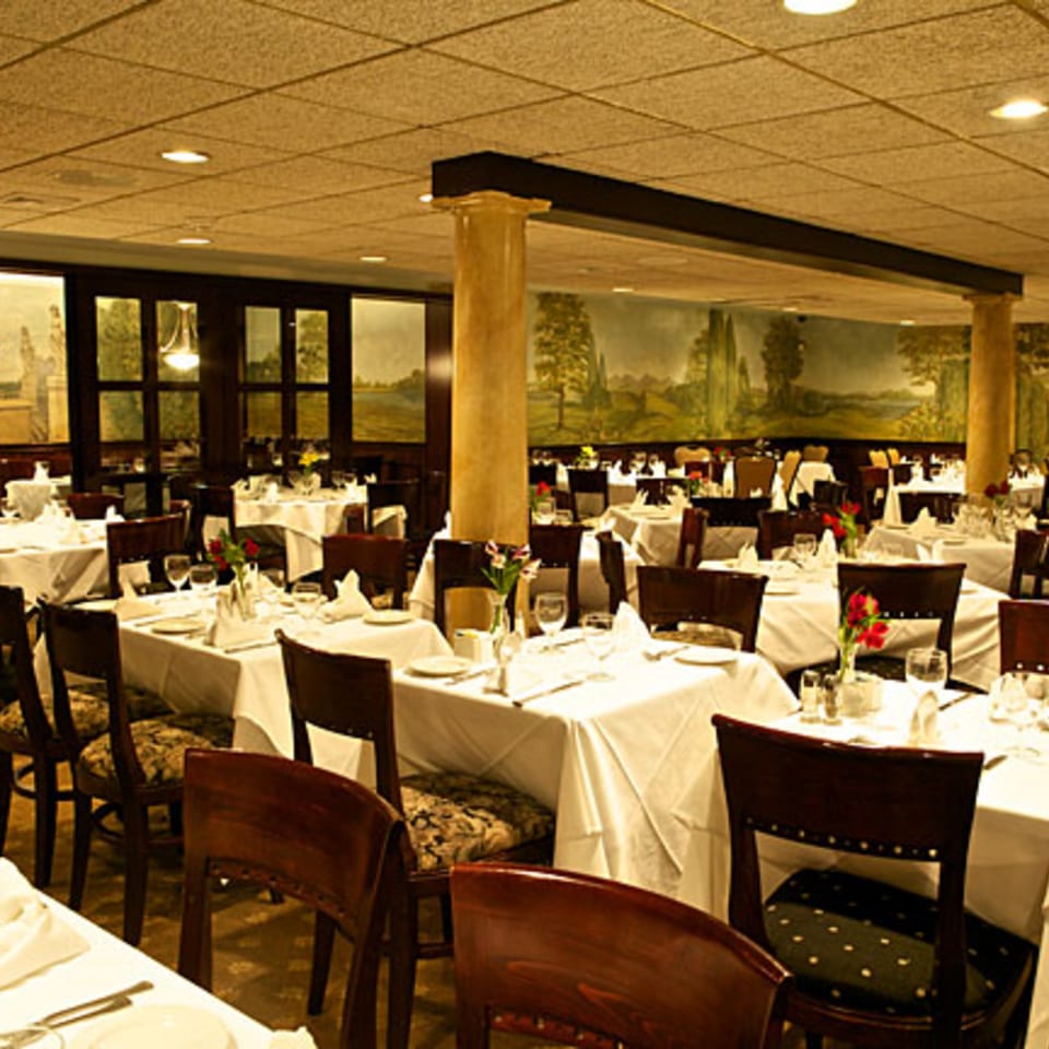 LouCas Italian restaurant dining room with white tablecloths, dark wood chairs, and scenic wall murals.