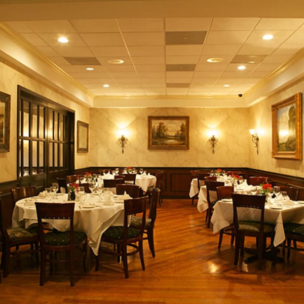 Elegant LouCas dining room with white-clothed tables, dark wood chairs, and warm lighting.