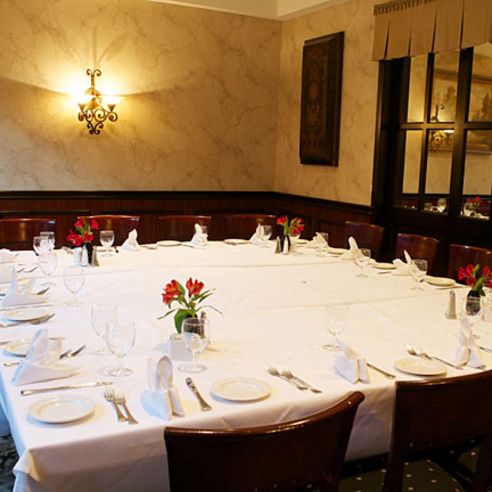 A private dining room at LouCas with a large, set table and red floral centerpieces.
