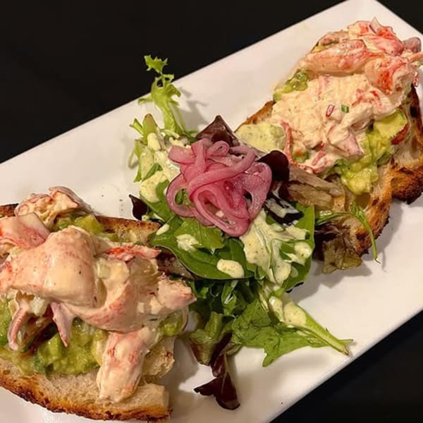 Two lobster and avocado toasts with a side salad topped with pickled red onions on a white plate.