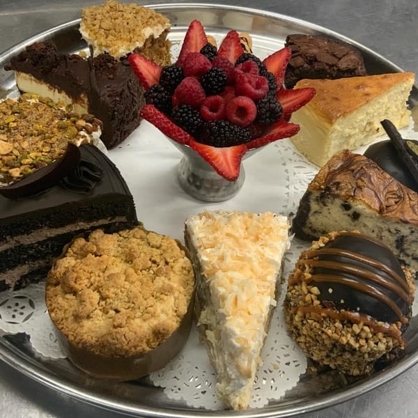 A silver platter filled with various LouCas Italian desserts, including cakes, cheesecakes, and fresh berries.